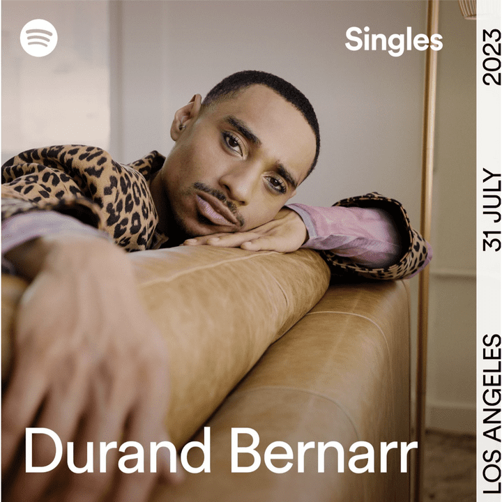 Durand is releasing new Spotify singles and here is a picture of himself staring into the camera on a sofa