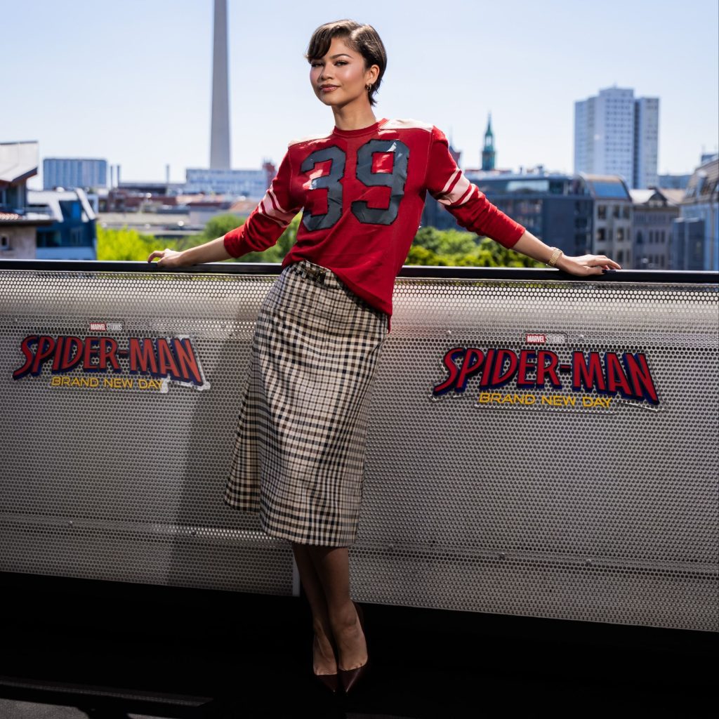 Zendaya wears a Coach Fall 2026 numbered long sleeve tee and a plaid skirt while doing press for Spider-Man: Brand New Day via 360 MAGAZINE.